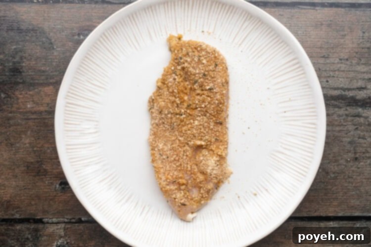 Breaded chicken cutlet resting on a large round white plate on a wooden table.