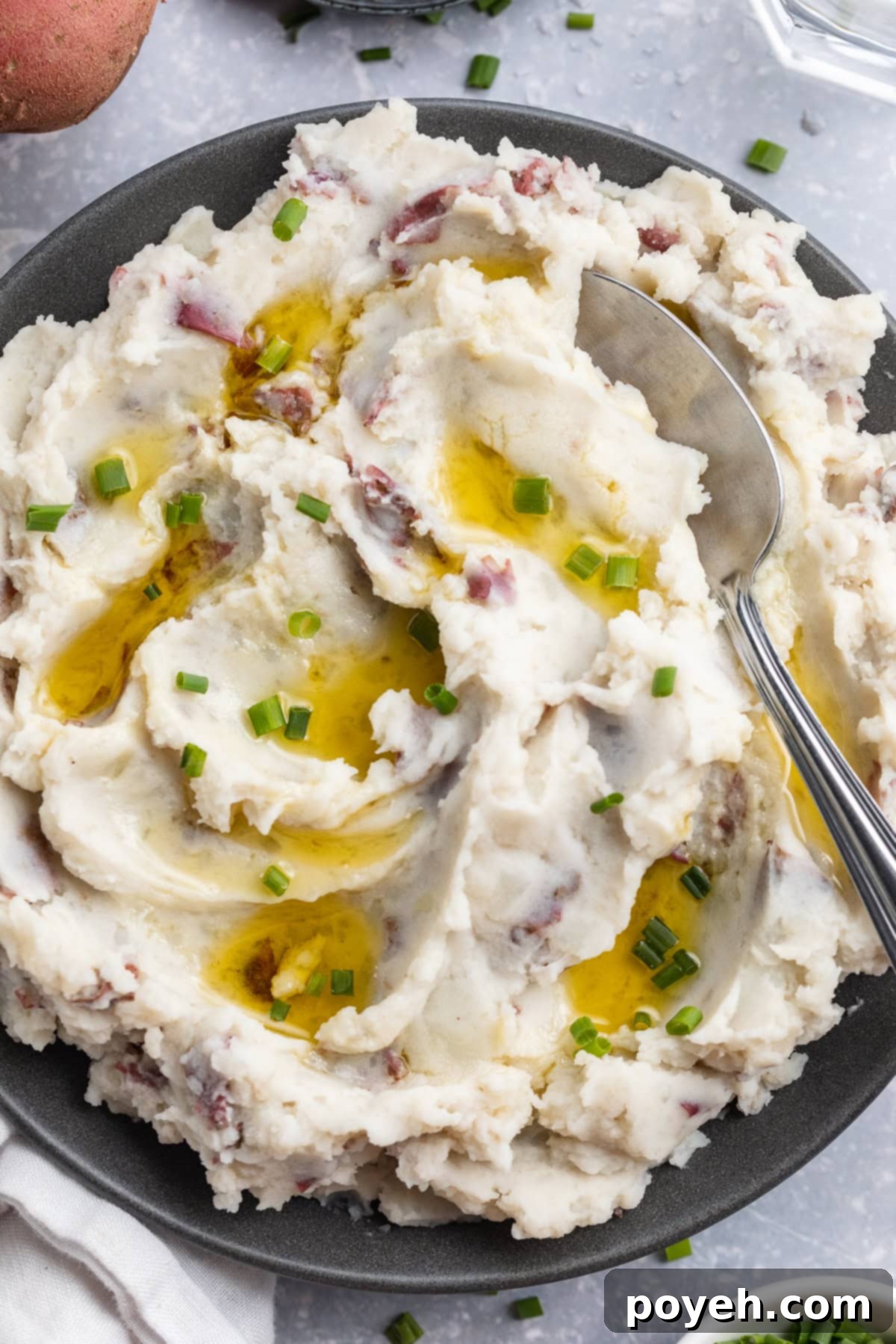Fluffy, whipped, red skin mashed potatoes in a large blue-grey bowl with a spoon on a holiday table.
