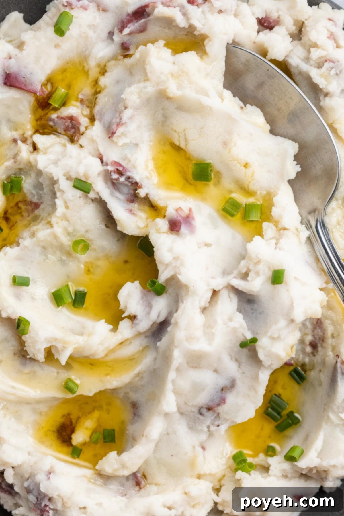 Fluffy, whipped, red skin mashed potatoes in a large blue-grey bowl with a spoon on a holiday table.