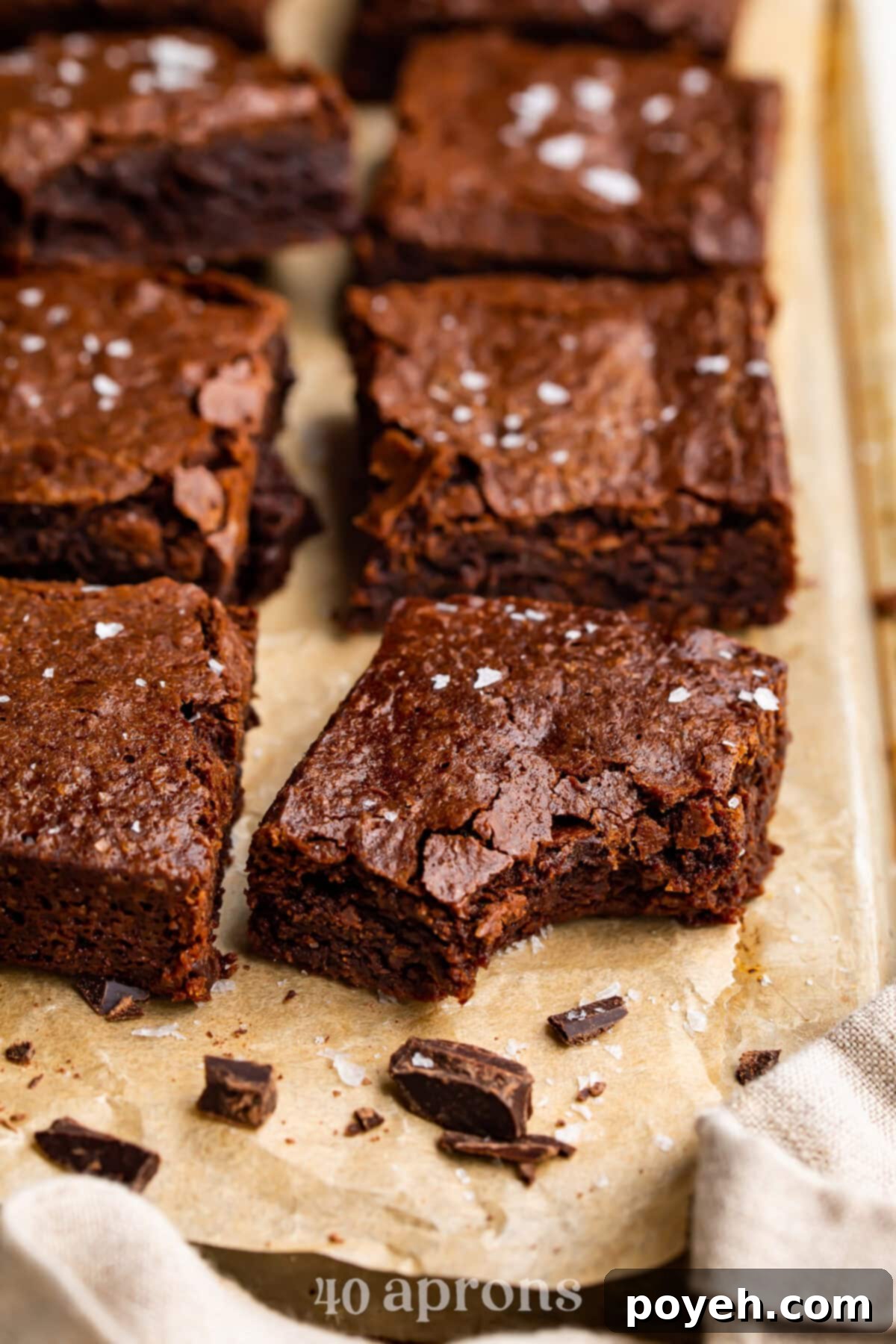 A dairy free brownie rests on a baking sheet covered in parchment paper. A bite is missing from the front corner of the brownie.