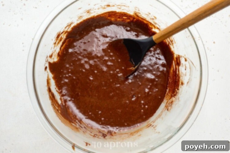 Brownie batter with chocolate chips folded in, sitting in a large glass mixing bowl with a silicone spatula.