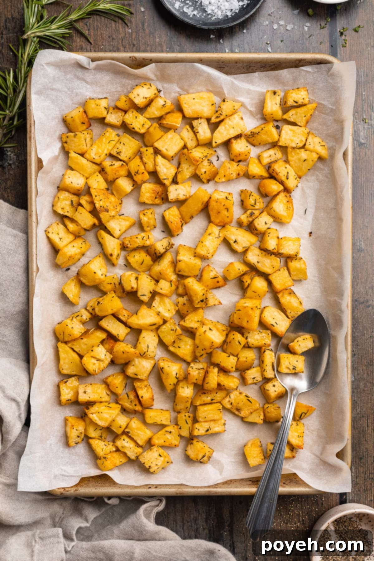 Overhead view of crispy golden diced potatoes spread evenly on a baking sheet lined with parchment paper, fresh out of the oven, highlighting their perfect texture.