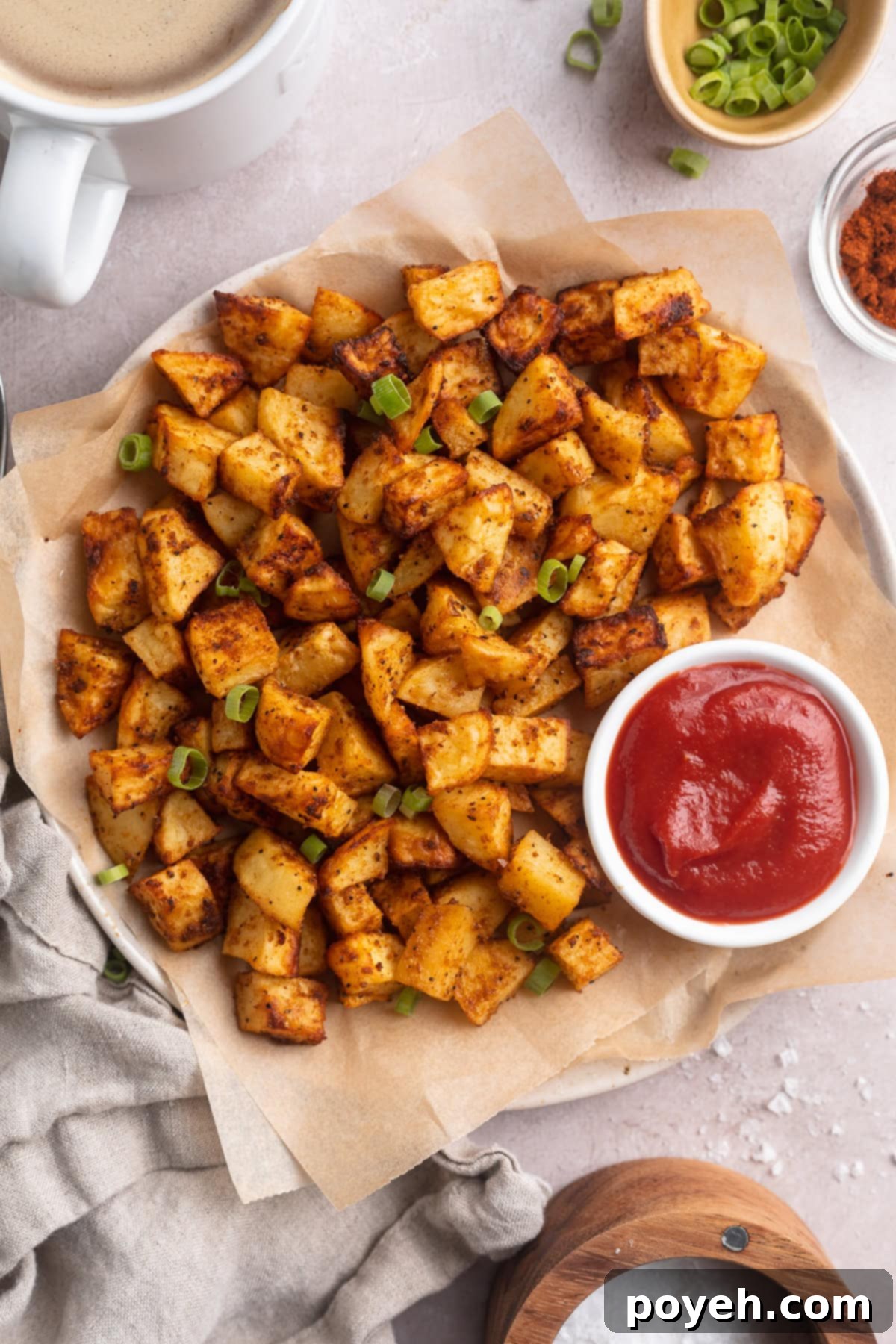 Overhead view of air fryer breakfast potatoes on a large round plate next to a ramekin of ketchup.