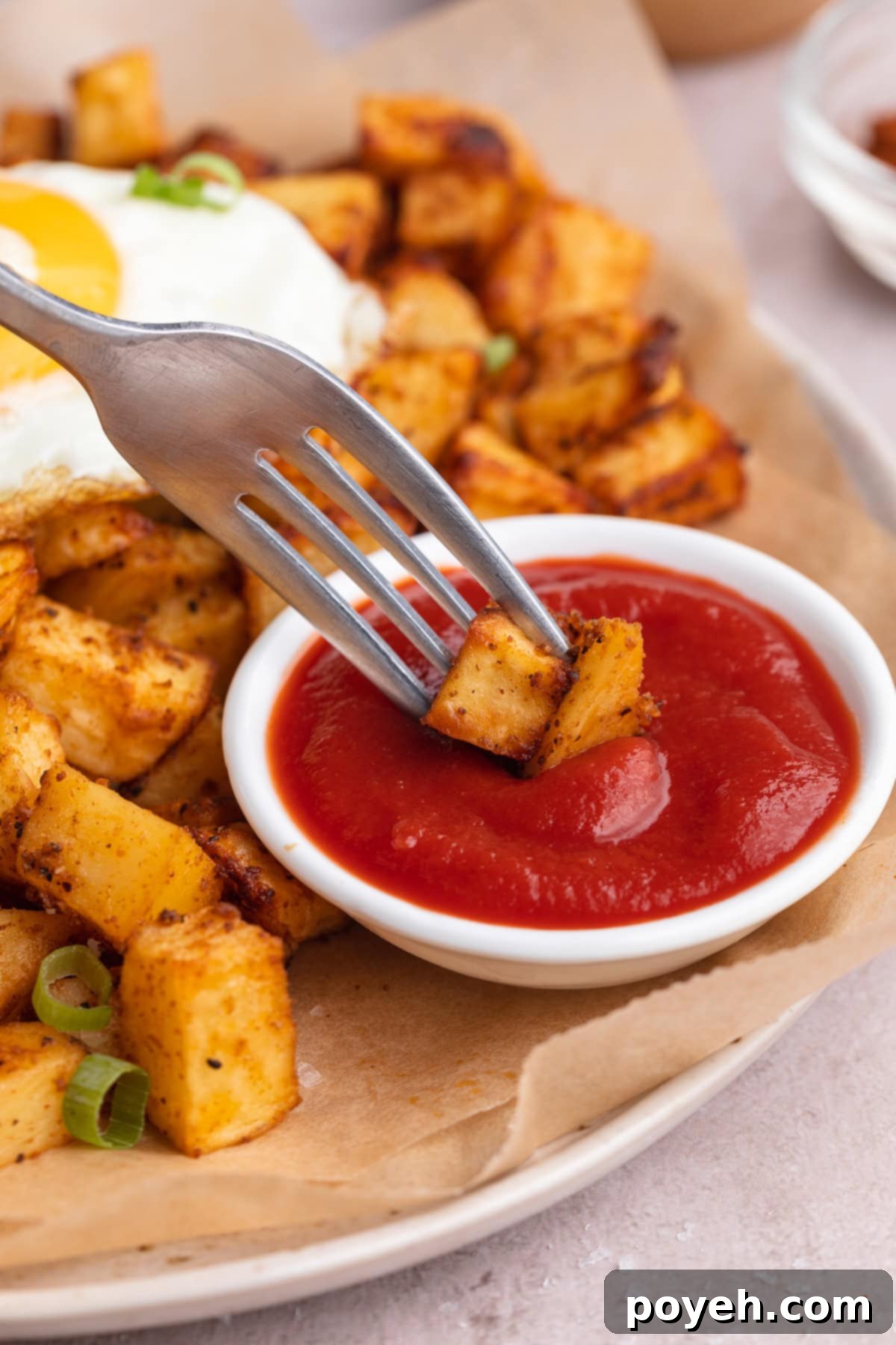 Air fryer breakfast potatoes on the end of a fork, being dipped into a small ramekin of ketchup.