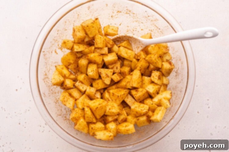 Overhead bowl with cubed potatoes, neutral oil, and several spices.