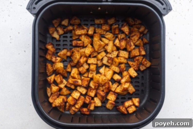 Overhead view of air fryer breakfast potatoes, fully cooked and golden brown, resting in an air fryer basket.
