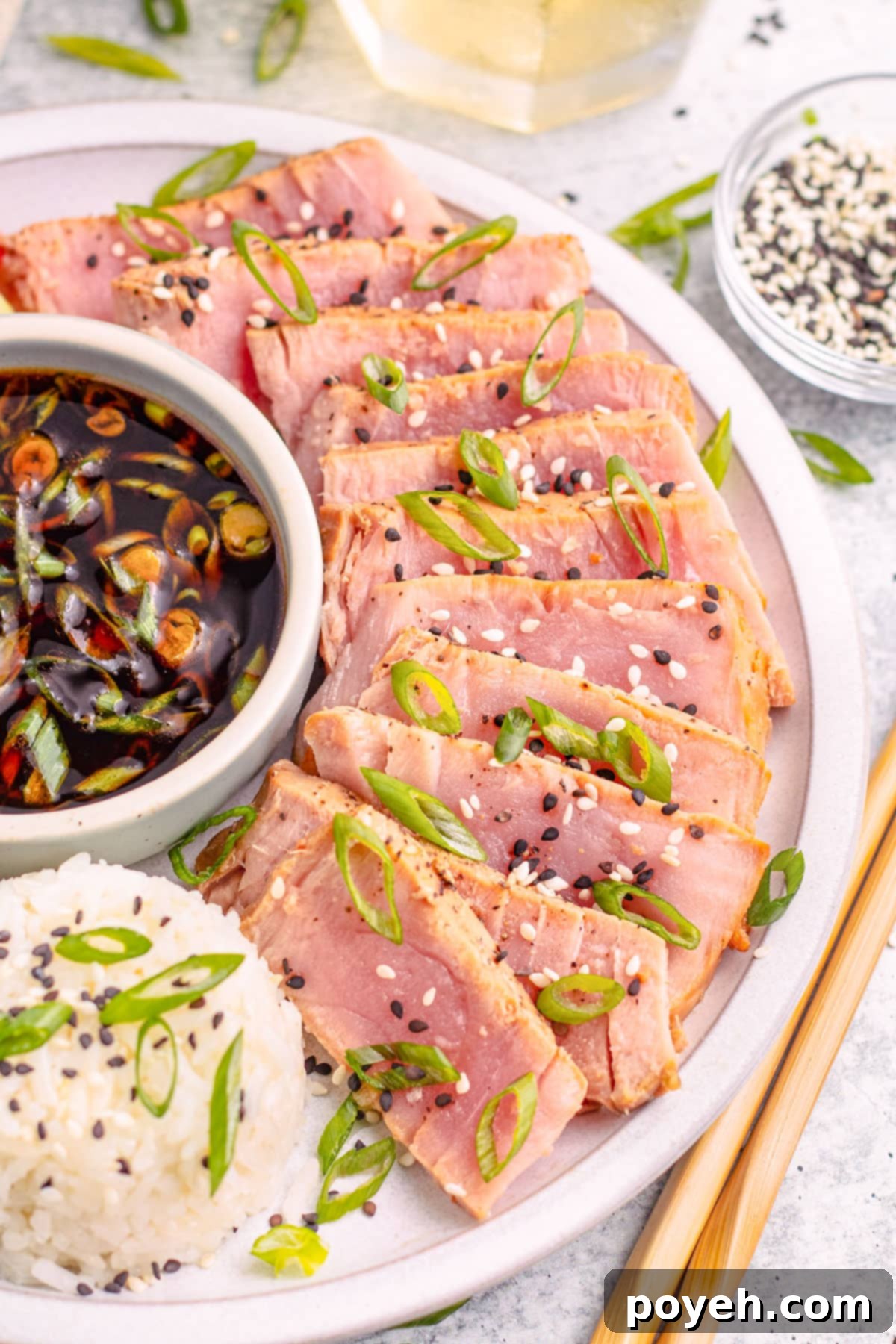 Air fryer tuna steaks, arranged in a semi-circle around a ramekin of soy sauce next to a mound of white rice garnished with sliced green onions.