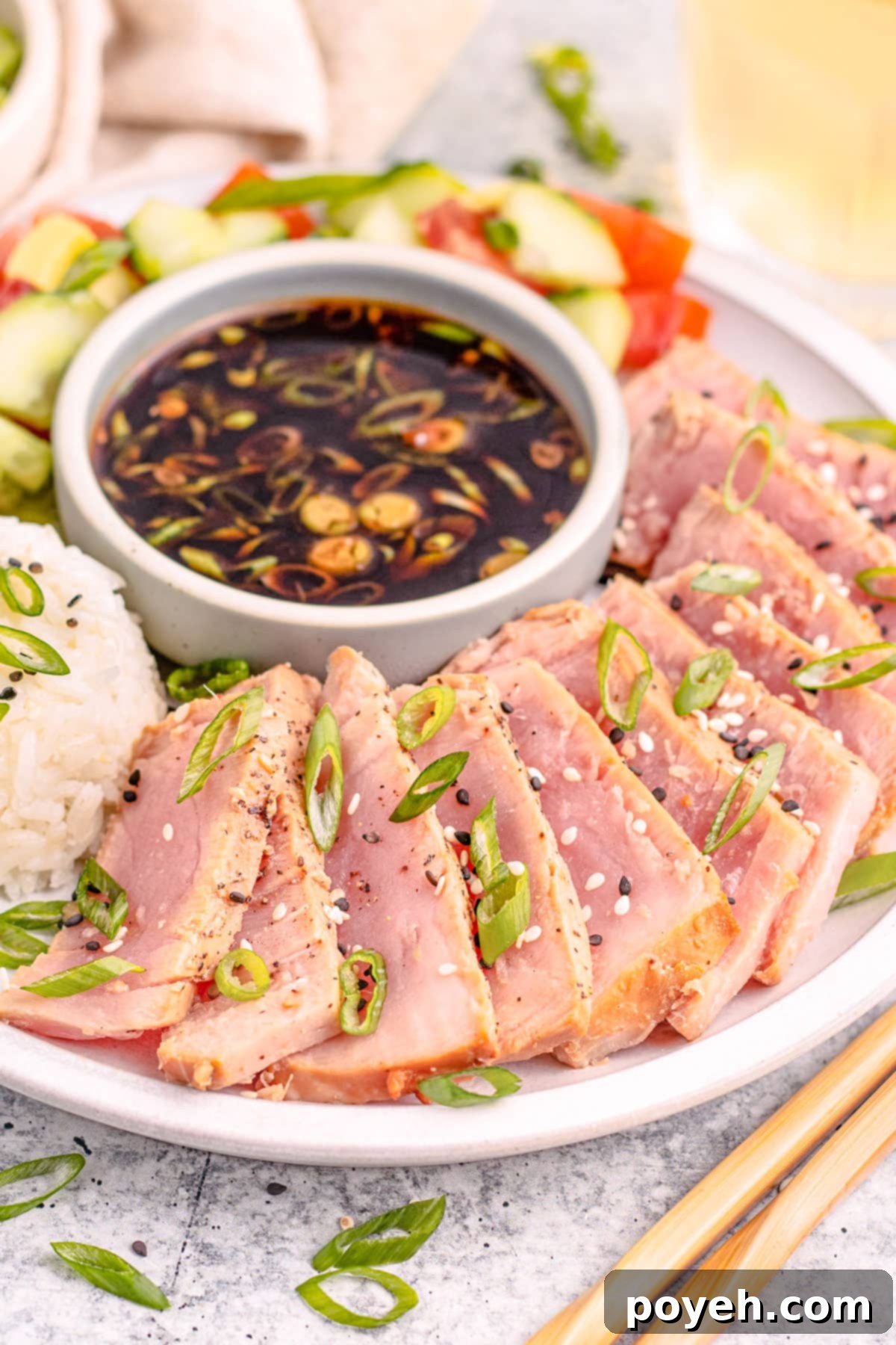 Air fryer tuna steaks, arranged in a semi-circle around a ramekin of soy sauce next to a mound of white rice garnished with sliced green onions.