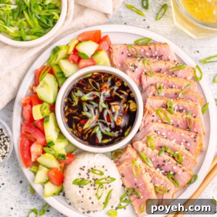 Air fryer tuna steaks, arranged in a semi-circle around a ramekin of soy sauce next to a mound of white rice garnished with sliced green onions.