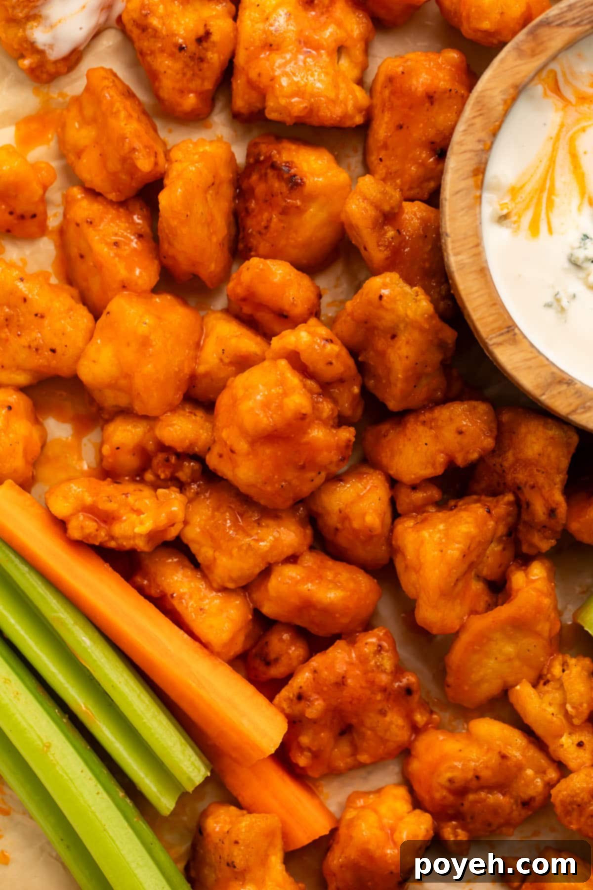 Crispy orange buffalo-sauce-covered tofu cubes on parchment paper, served with ranch dressing and celery sticks.