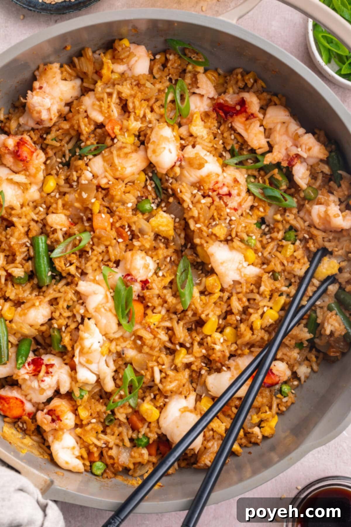 Close up photo of a grey bowl holding lobster fried rice with veggies and chopsticks.
