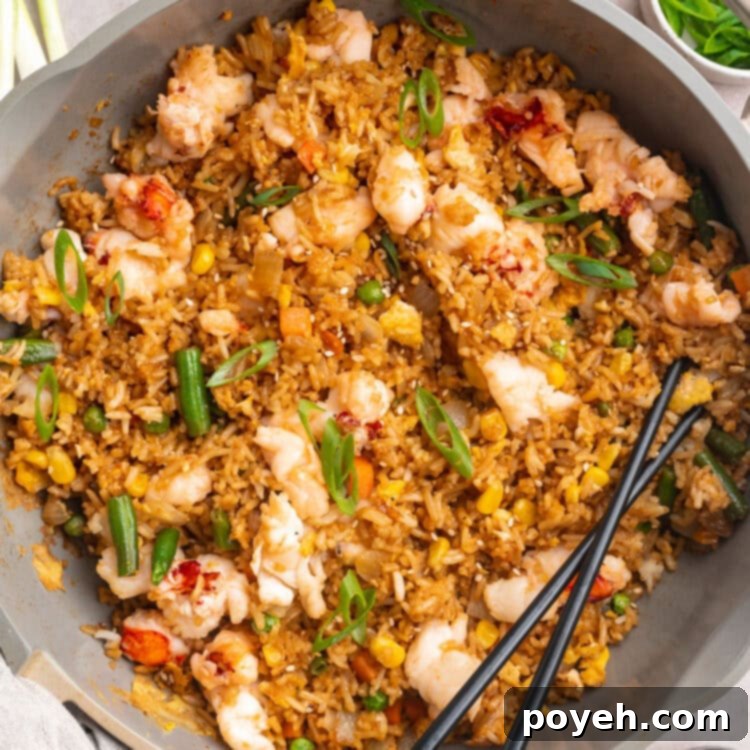 A large grey shallow bowl holding lobster fried rice with veggies and a set of black chopsticks resting on the edge of the bowl.