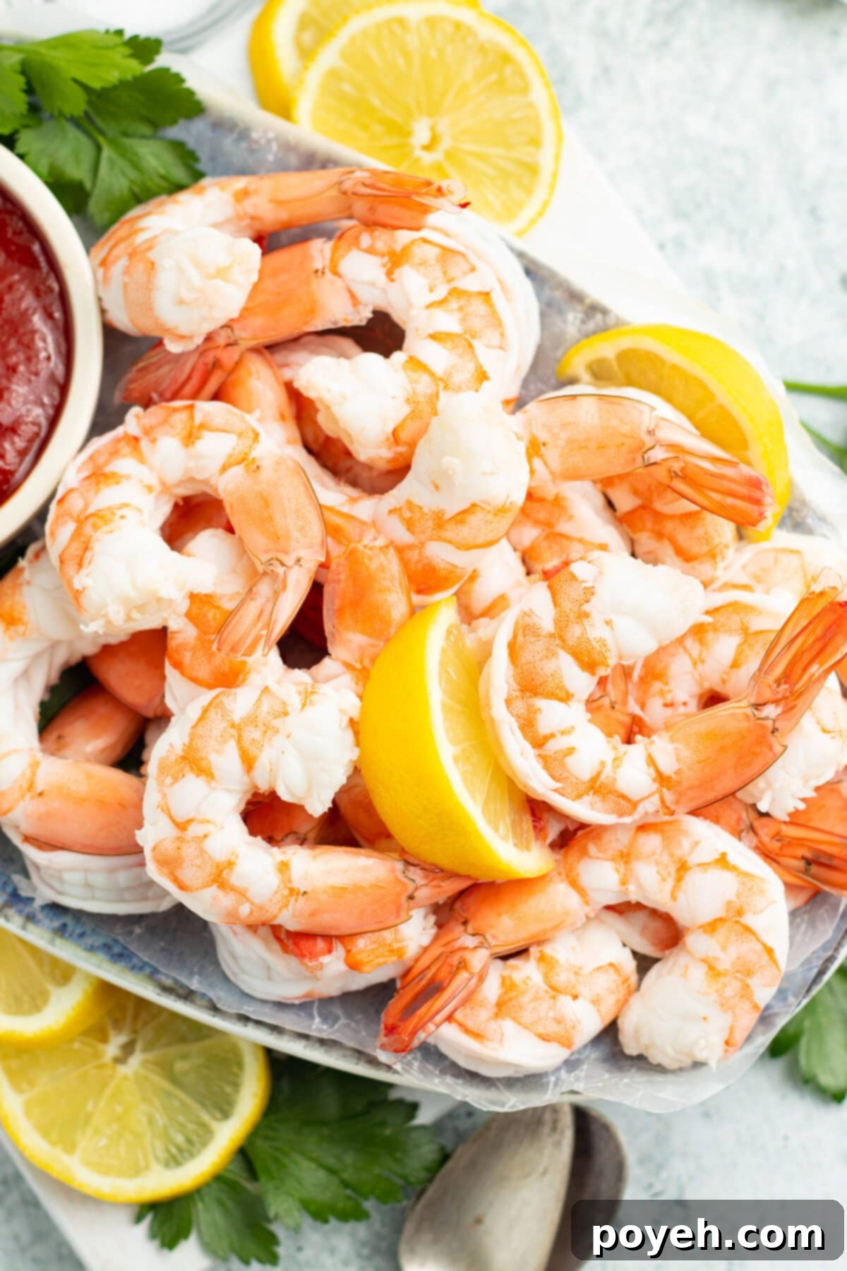 An overhead view of perfectly poached shrimp arranged on a bed of ice, garnished with vibrant lemon wedges and a side of dipping sauce, ready to serve.