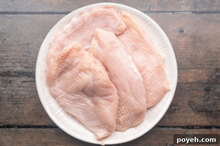 Raw chicken breasts on a round white plate, ready for pounding.
