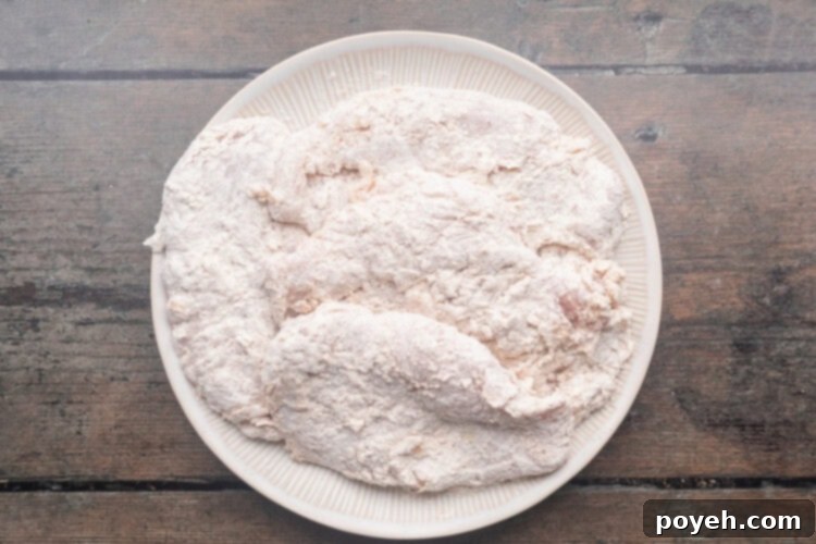 Breaded chicken breasts on a round white plate, ready for frying.