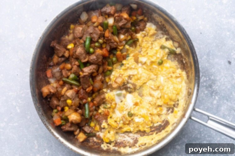 Duck breast, soy sauce, spices, and frozen mixed vegetables in a large silver skillet with half the pan holding scrambled eggs.
