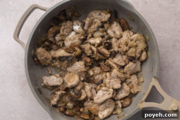 Strips of pork tenderloin in large skillet with sautéed mushrooms and diced onions.