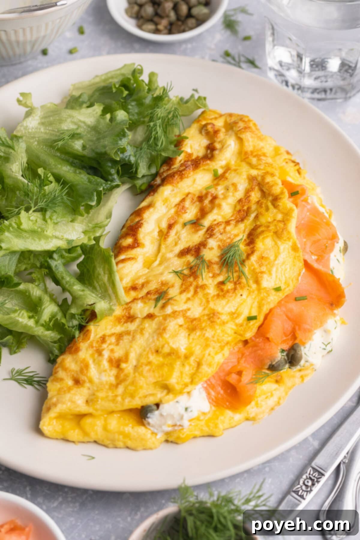 Overhead view of a beautifully folded smoked salmon omelette served on a plate with a fresh green salad, highlighting its rich textures and vibrant colors.