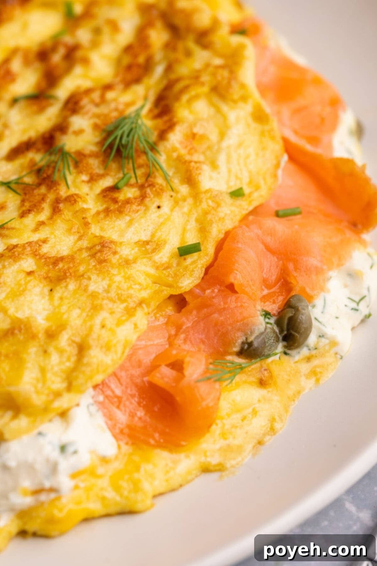 Close-up detailed view of a folded smoked salmon omelette on a white plate, garnished with fresh herbs and served alongside a vibrant green salad.