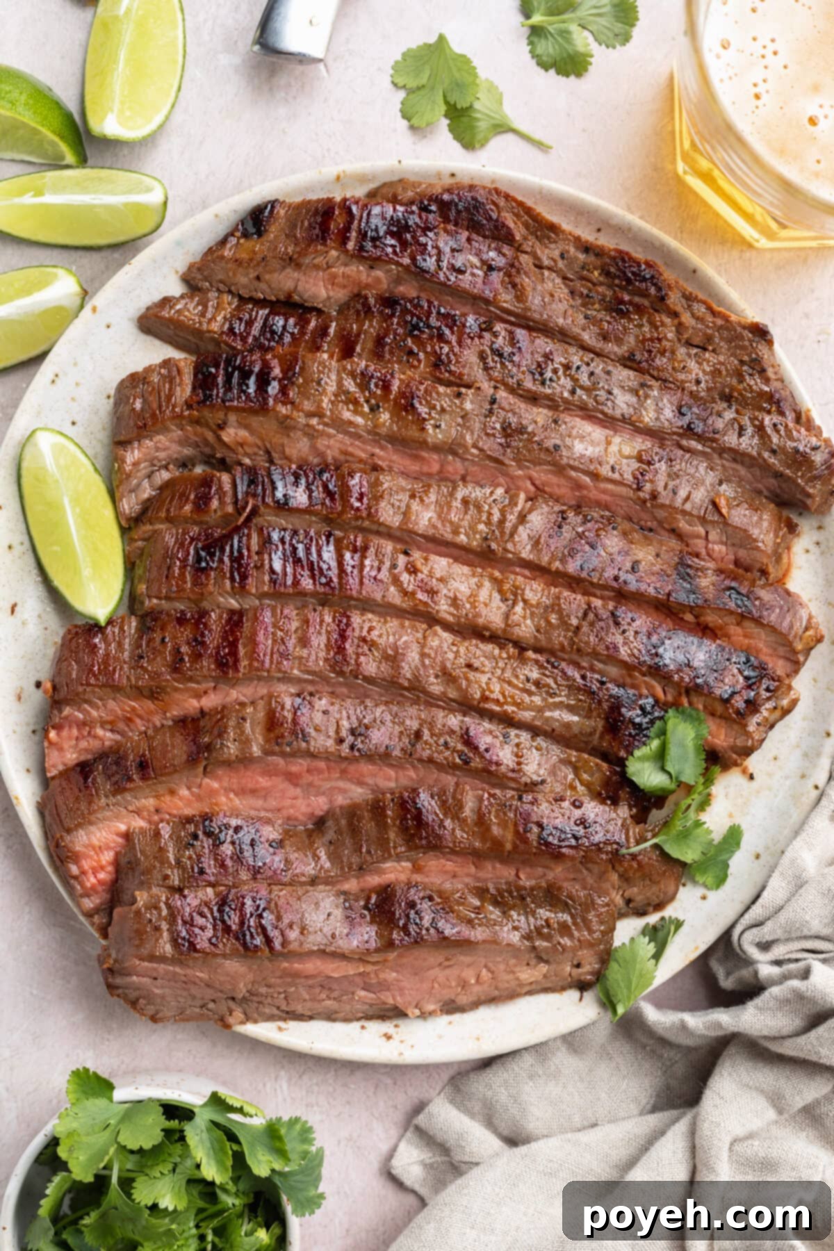 Top-down view of a sliced, sous-vide cooked flank steak on a white plate surrounded by lime wedges and other garnish.