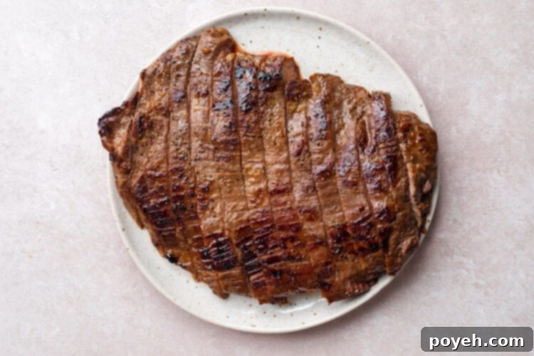 Seared flank steak on a white plate. Steak has been sliced into thick pieces.