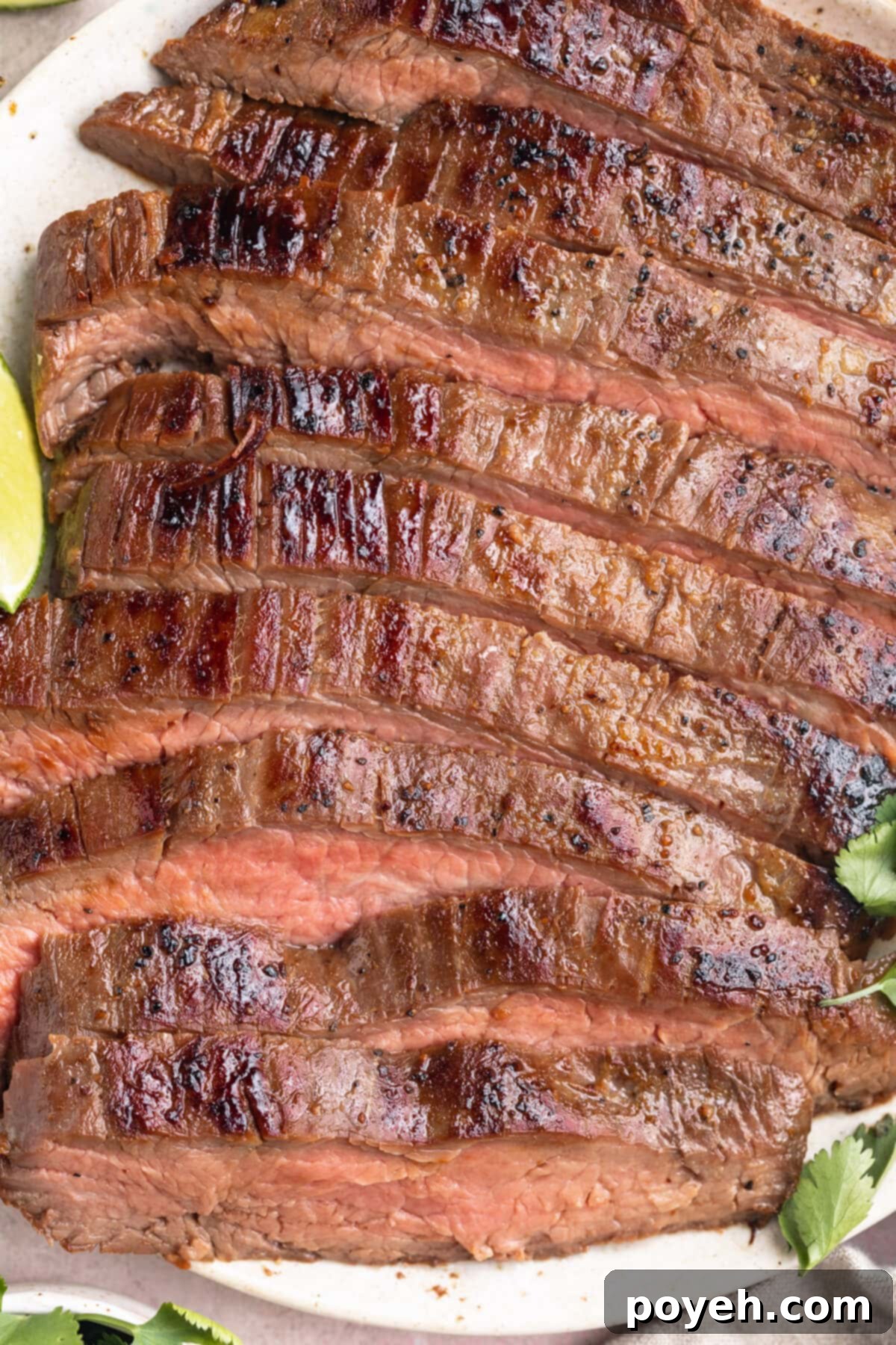 Close-up view of thickly sliced sous vide flank steak on a white plate with lime wedges.