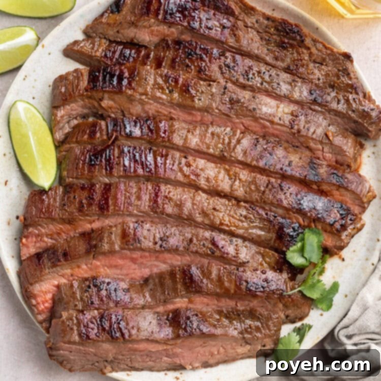 Top-down view of a sliced, sous-vide cooked flank steak on a white plate surrounded by lime wedges and other garnish.