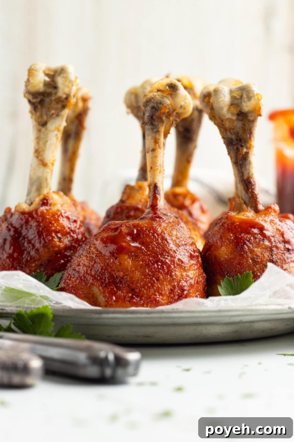 Side view of perfectly glazed lollipop chicken legs, standing upright on a baking sheet lined with parchment paper, showcasing their unique and appealing presentation.