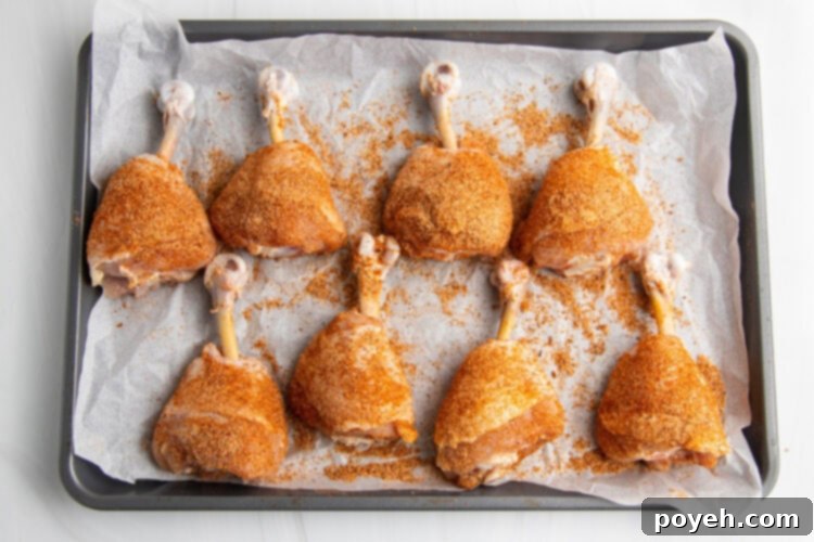 Dry rub seasoned drumsticks laying on a baking sheet lined with aluminum foil.