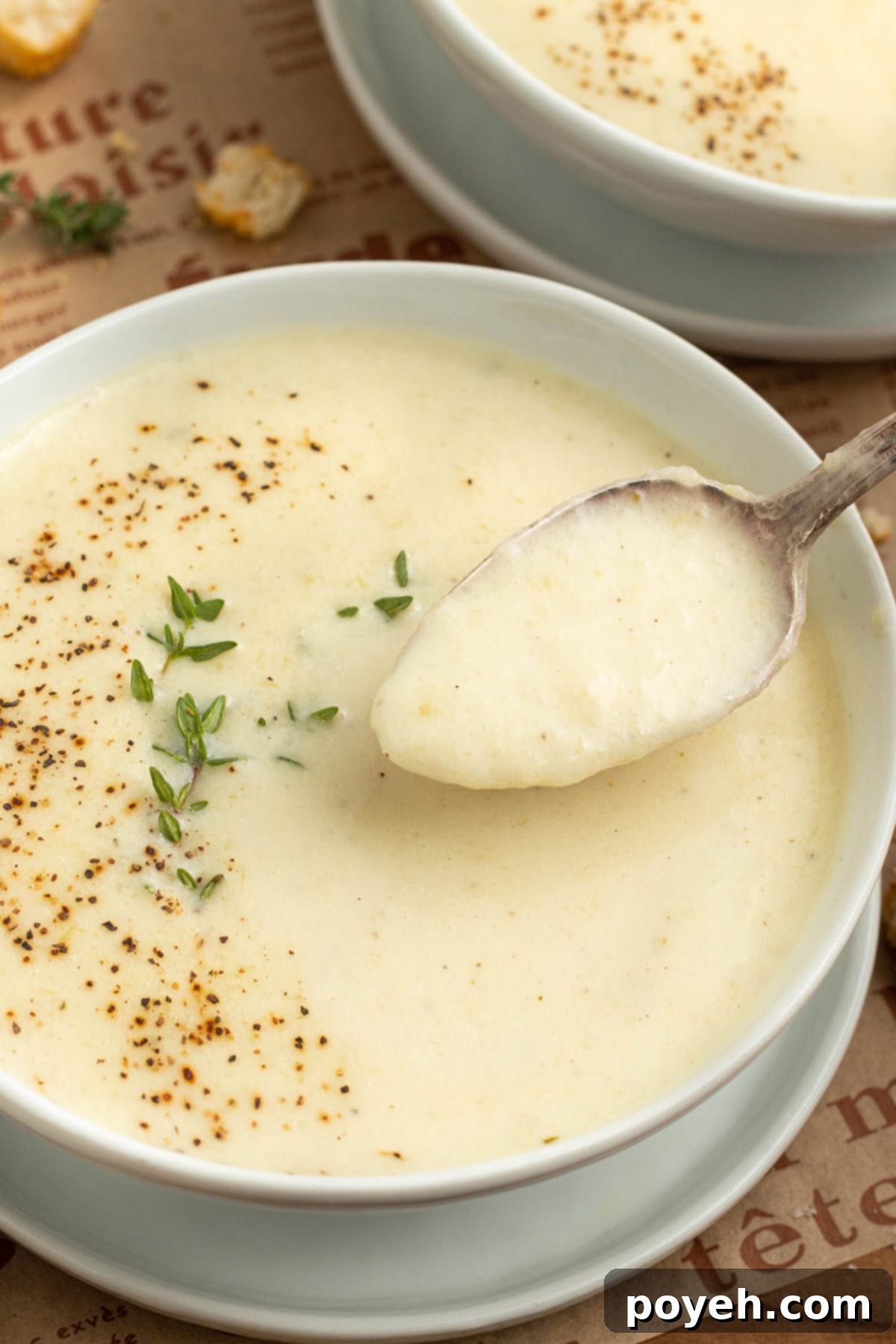 A spoonful of cream of onion soup being lifted out of a white bowl of soup.
