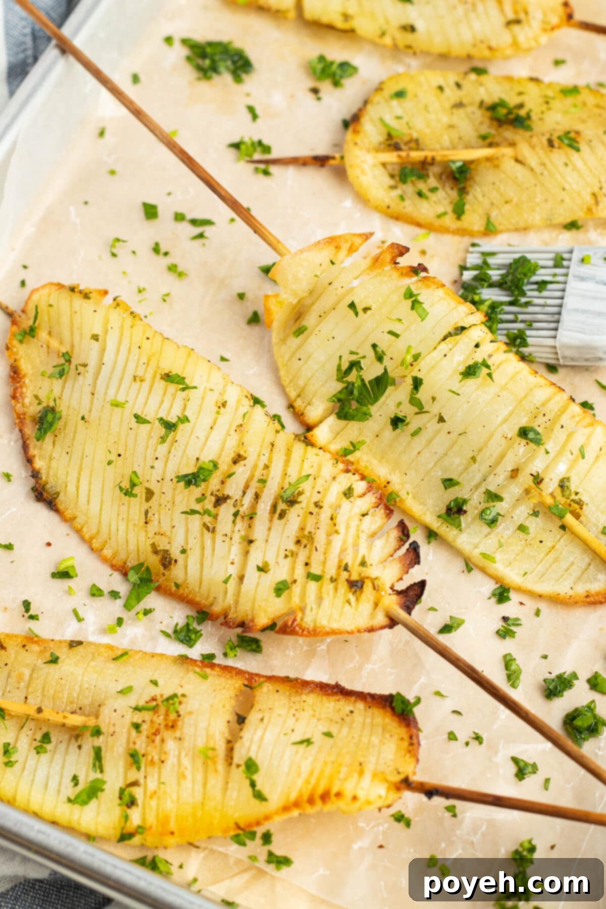 Skewered accordion potatoes arranged on parchment paper, golden brown and crispy.