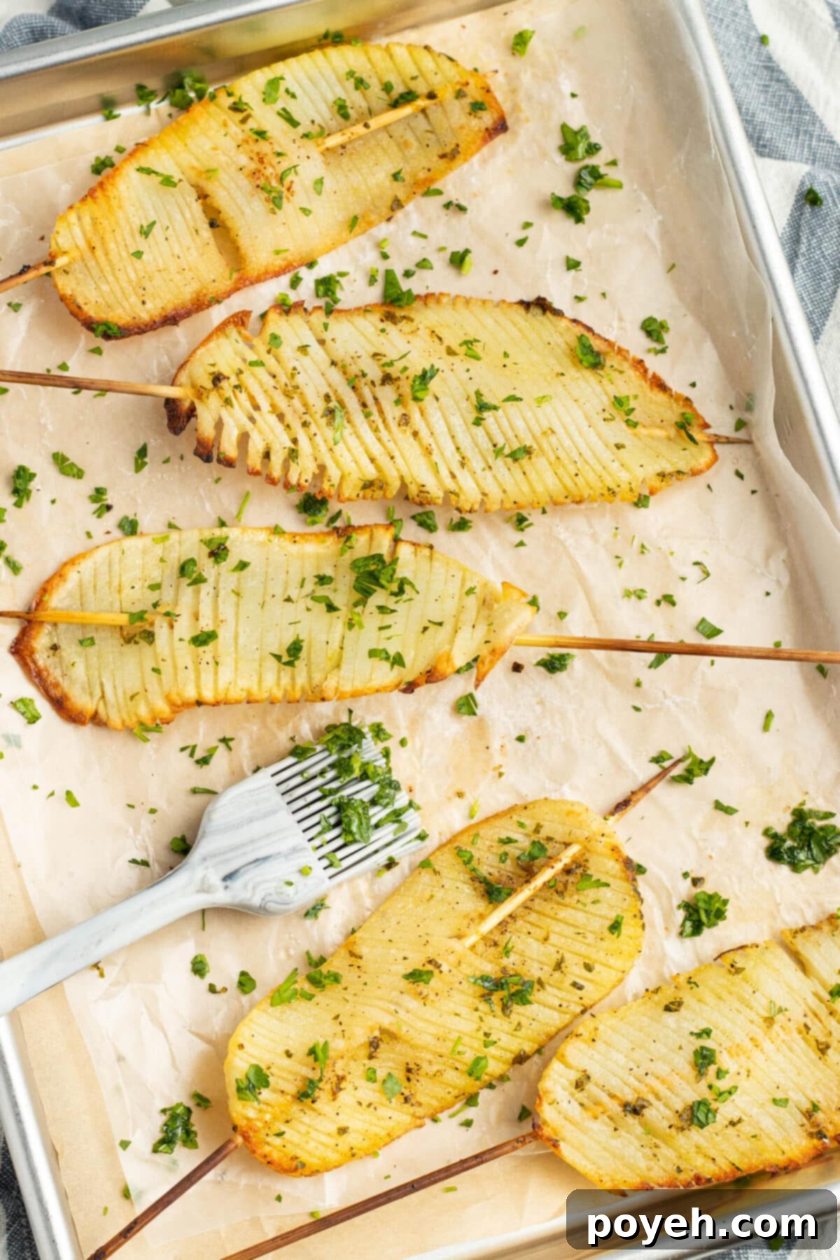 Close-up of golden brown accordion potatoes on skewers with fresh parsley garnish.