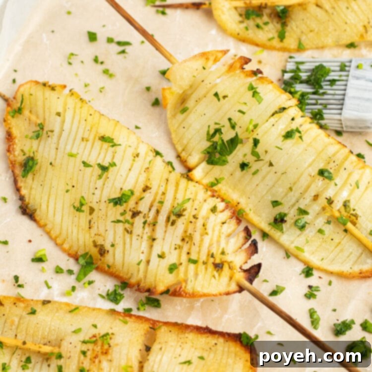 Perfectly baked accordion potatoes on skewers, garnished with fresh herbs.