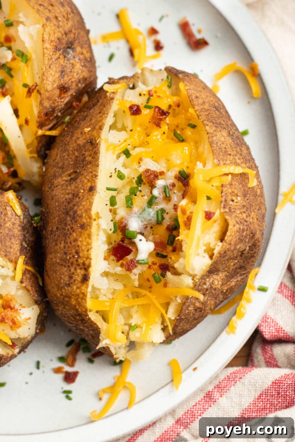 Overhead view of a smoked baked potato topped with cheese and bacon on a white plate.
