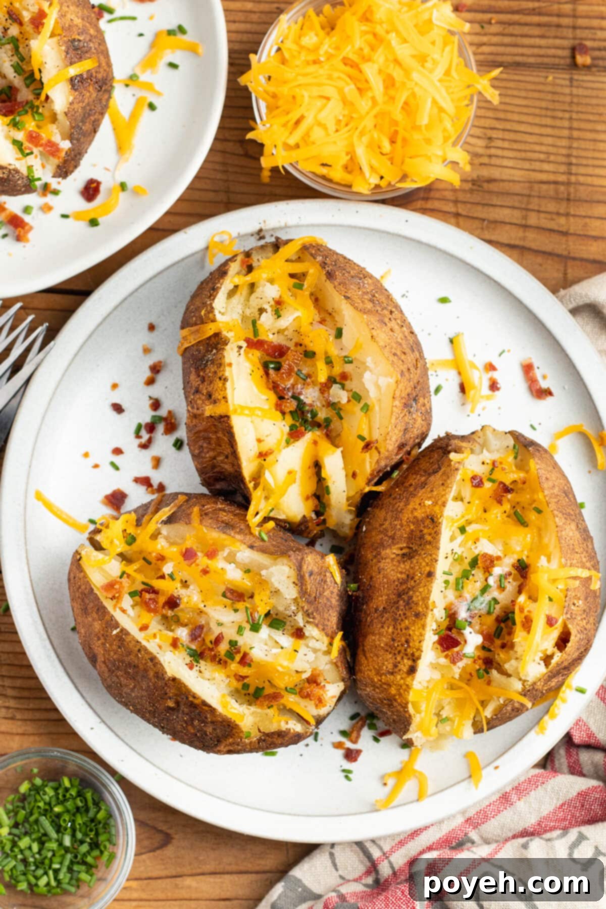 Three smoked baked potatoes sliced open and topped with cheese and bacon, arranged on a white plate.