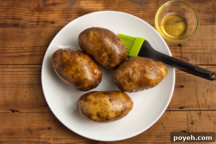 Olive oil being brushed onto 4 russet potatoes with a basting brush.