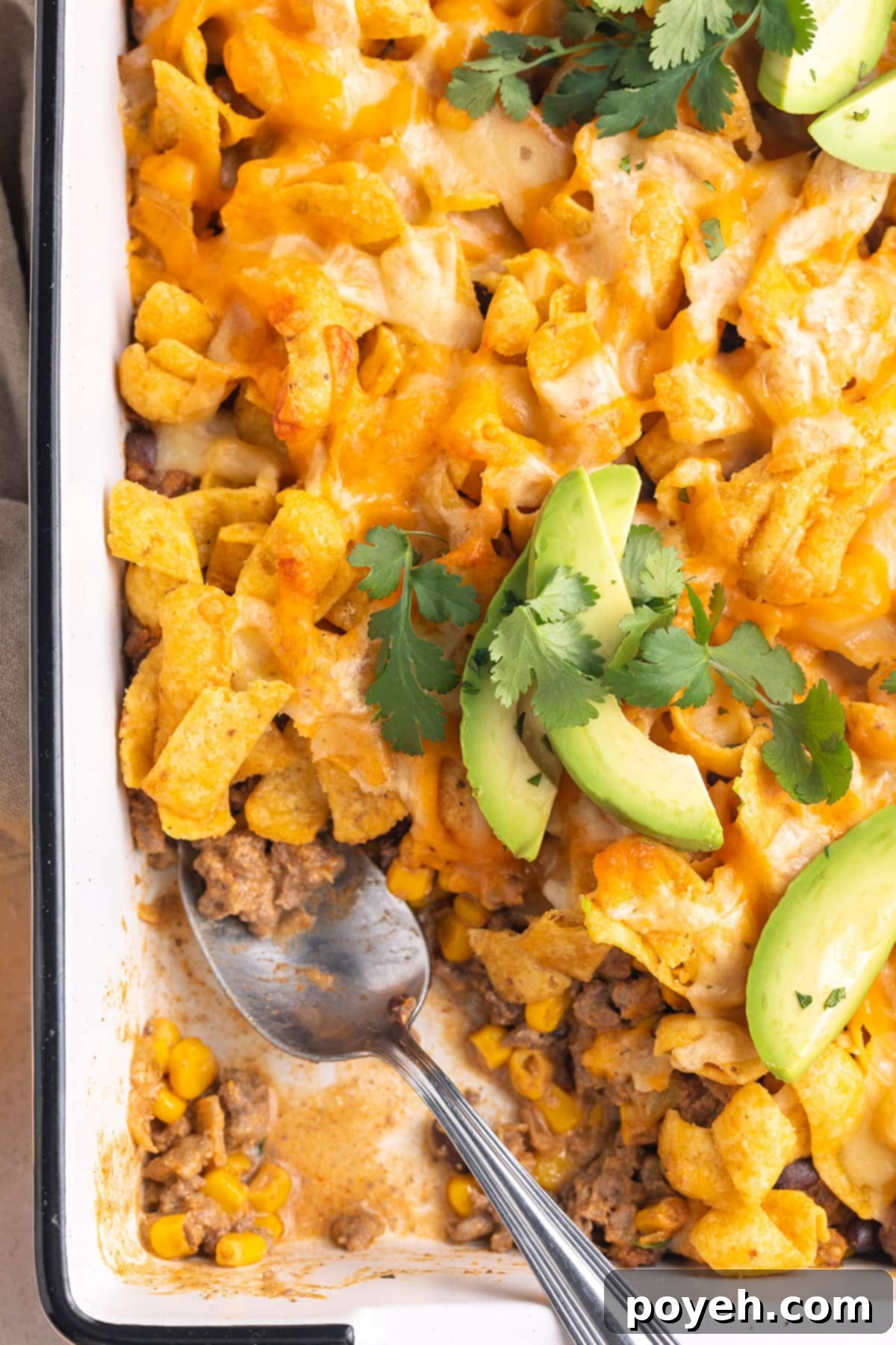 Walking taco casserole in a rectangular white casserole dish. A scoop is missing.