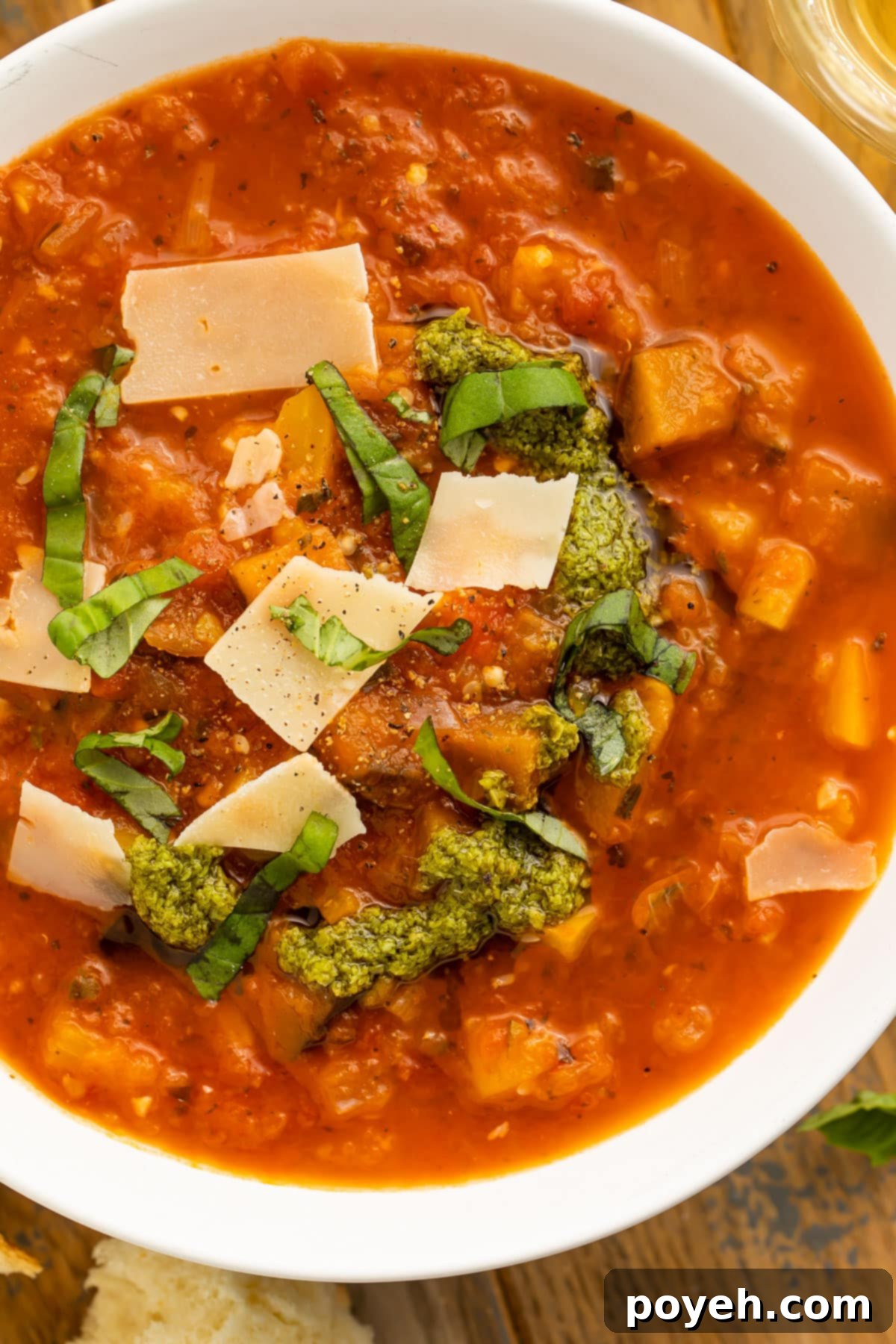 Close-up of a bowl of ratatouille soup topped with fresh basil leaves and parmesan, ready to be enjoyed.