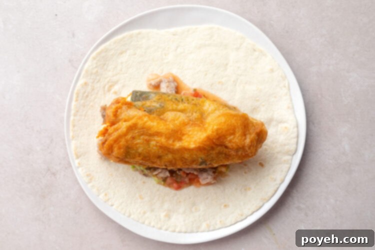 An unrolled chile relleno burrito showcasing all its delicious fillings: guacamole, pico de gallo, carnitas, and a chile rellano on top.