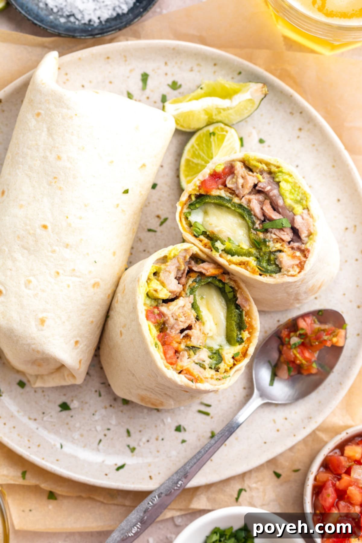 Overhead view of a chile relleno burrito cut in half and stood up on a plate, next to a whole burrito, garnished with fresh cilantro.