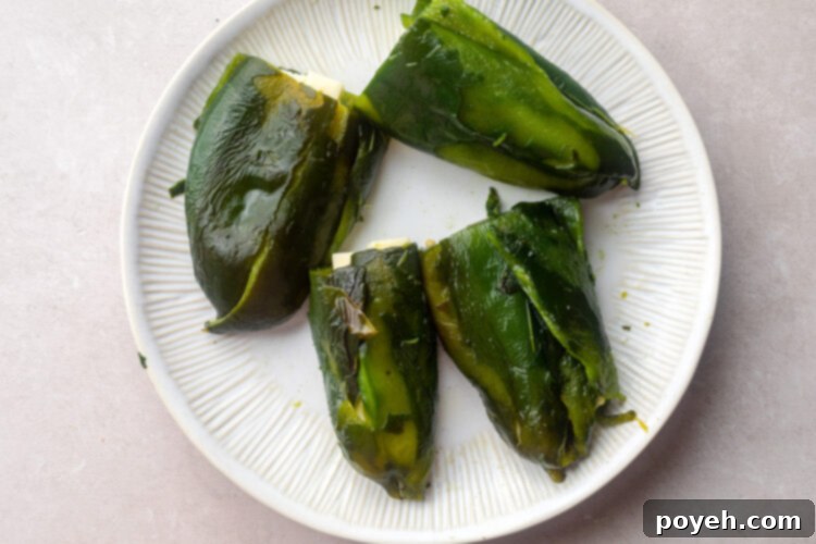 Charred poblano peppers generously stuffed with Monterey Jack cheese on a white plate, ready for breading.
