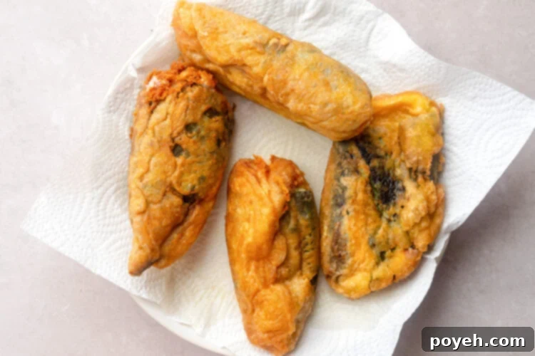 Freshly fried chile rellenos on a large white plate with paper towels, cooling and draining excess oil.
