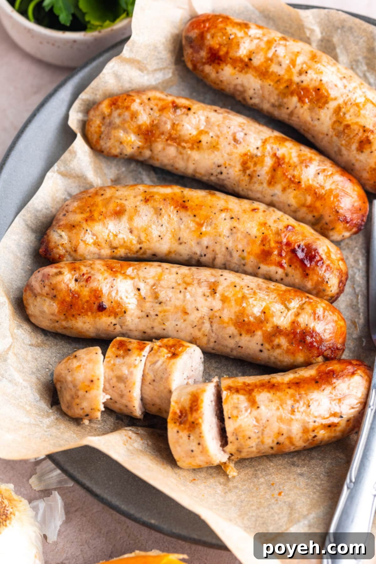5 Italian sausages on a plate lined with parchment paper. One of the sausages is sliced into thick discs.