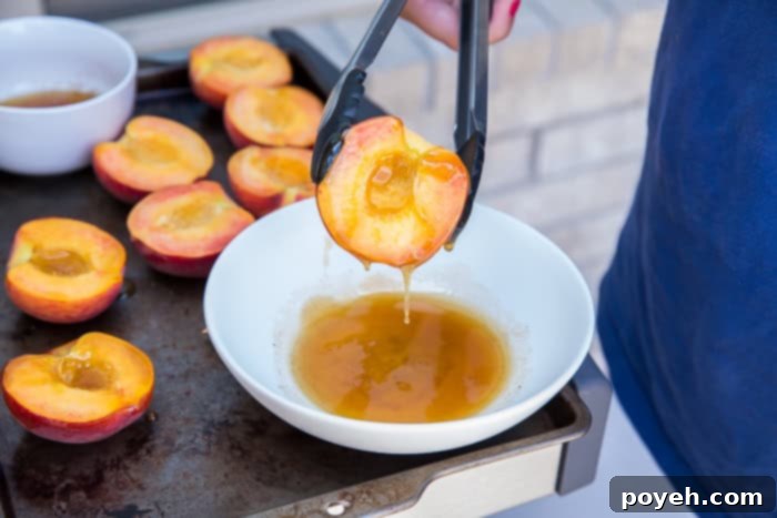 A peach half being dipped in honey for grilling