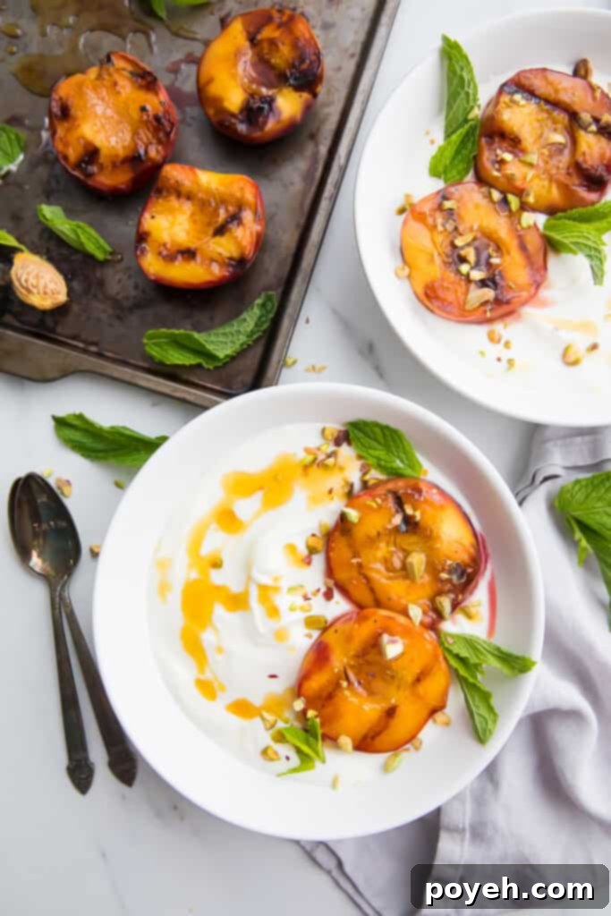 Grilled peaches served on two white plates and drizzled with honey, garnished with mint