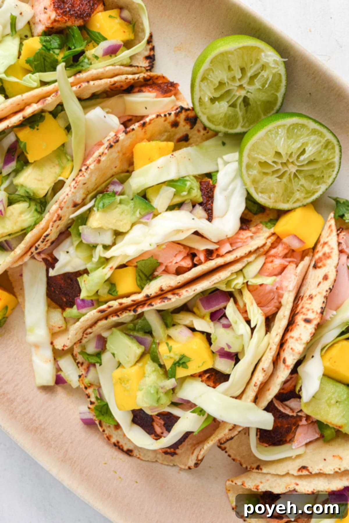 4 salmon tacos topped with slaw and mango salsa on an oval platter.