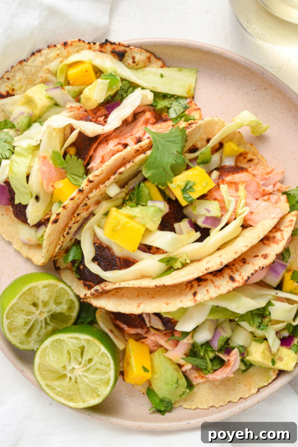 3 salmon tacos topped with mango salsa and fresh cabbage slaw on a round plate.