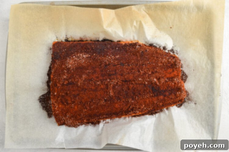 Seasoned salmon fillet on a baking sheet lined with parchment paper.