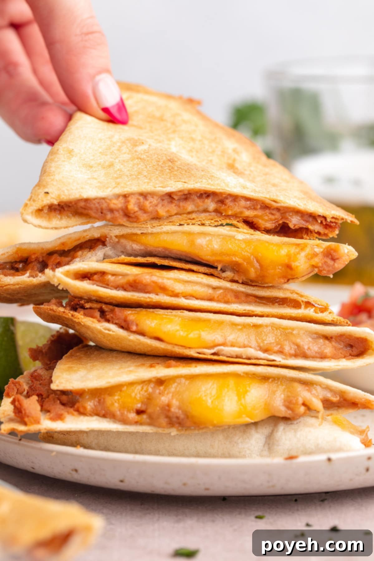 A white woman's hand picking up a triangular quesadilla slice from a stack of crispy air fryer quesadilla slices on a plate.