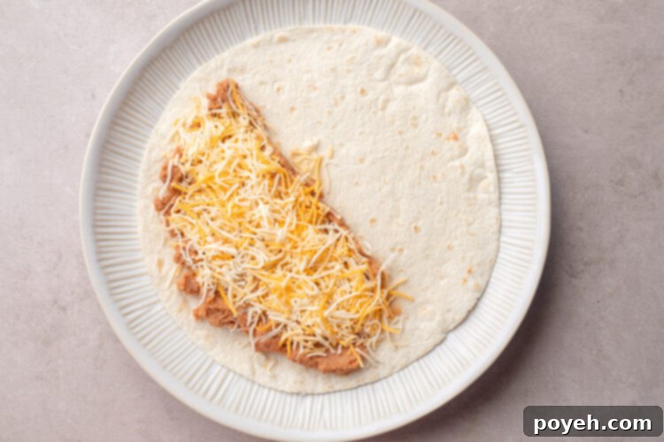 Refried beans and shredded cheese on one half of a 10-inch flour tortilla on a plate.